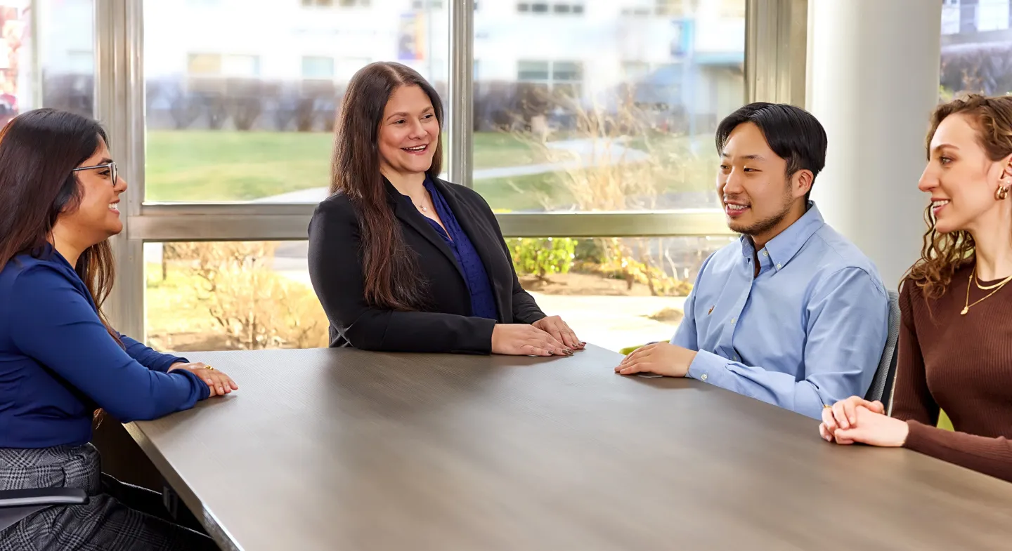 Four colleagues sitting at a table in discussion with smiles in a sunlit conference room