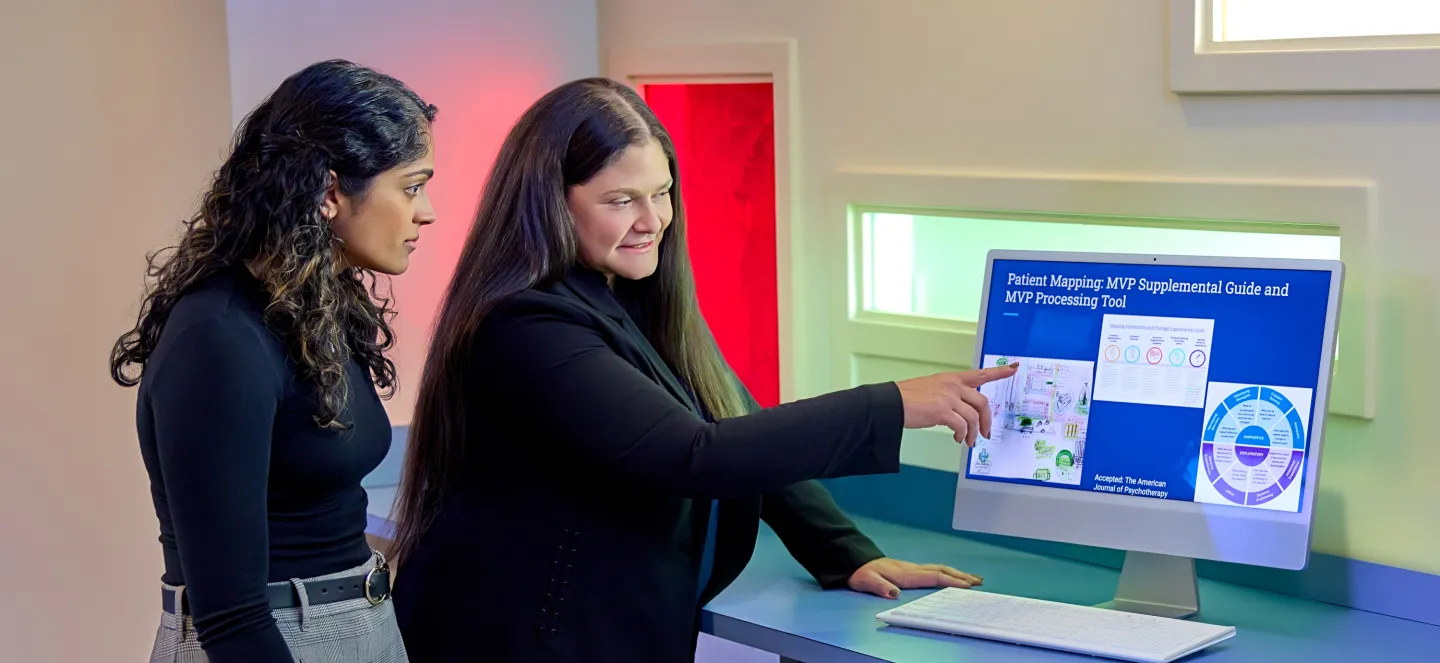 Two women viewing a computer screen displaying a patient mapping guide and therapy tool in a modern office