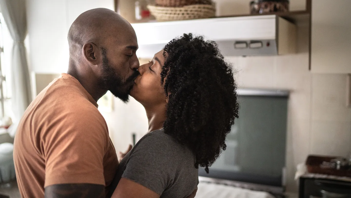 Couple sharing a kiss in a cozy kitchen, embracing each other lovingly.