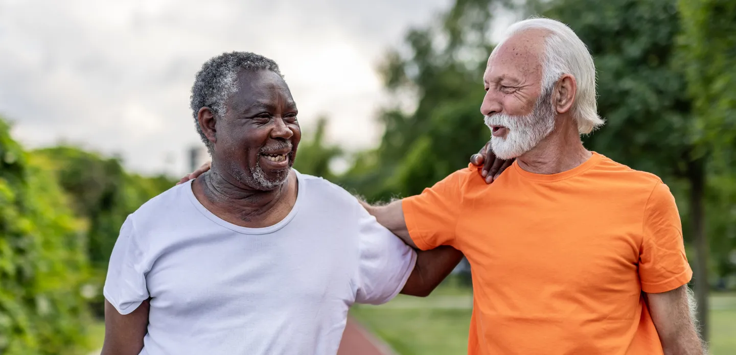 Two older men smiling and walking together outdoors, arms around each other in friendly support.