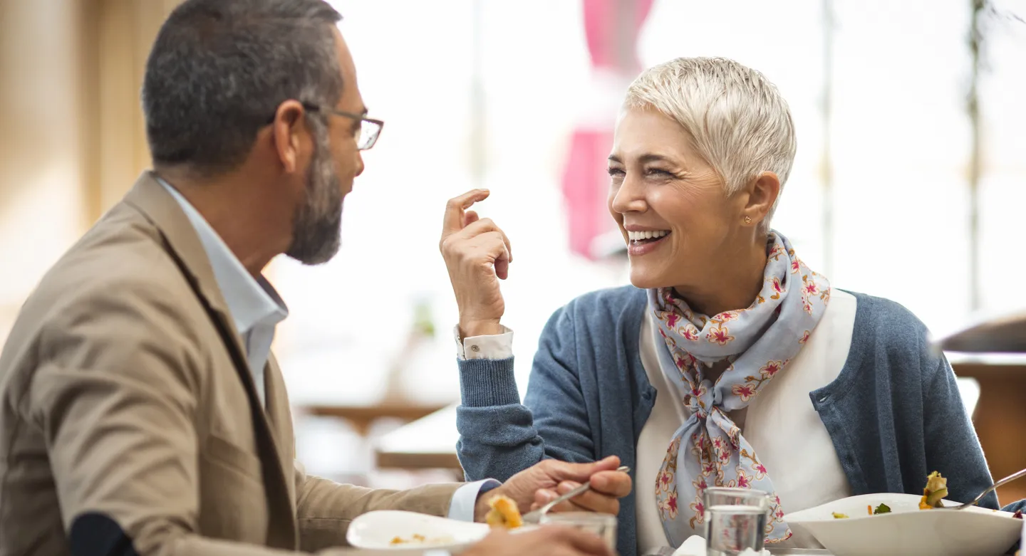 Smiling mature couple enjoys a meal together at a restaurant, engaged in lively conversation.