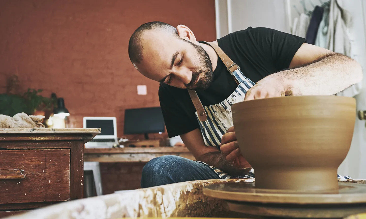 Man focused on shaping a large clay bowl on a pottery wheel in a workshop studio.