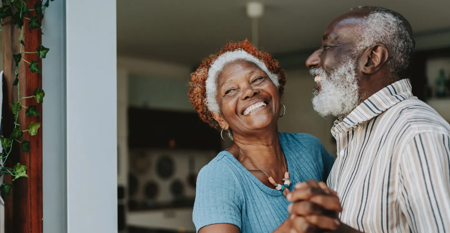 Smiling older couple dancing together indoors, holding hands and laughing.