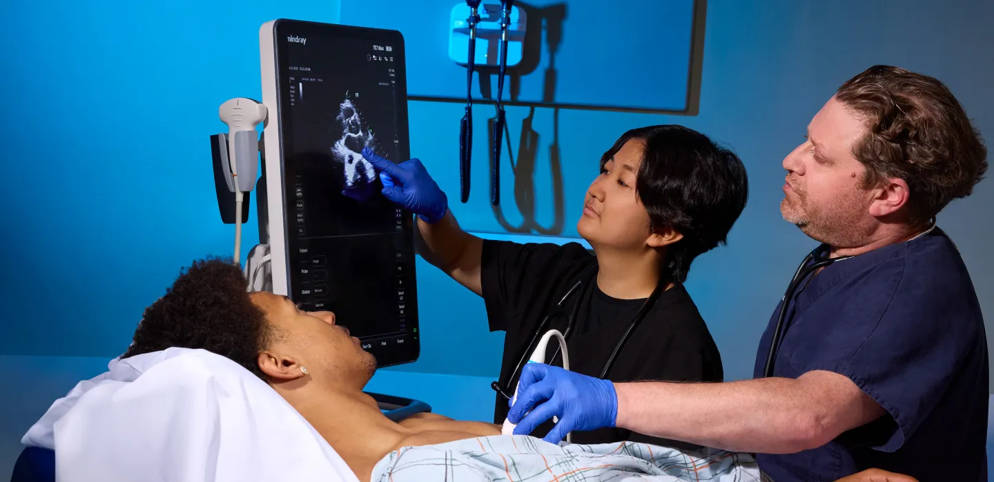 Medical student and physician use ultrasound device to examine a patient in a hospital room, highlighting diagnostic training and bedside care.