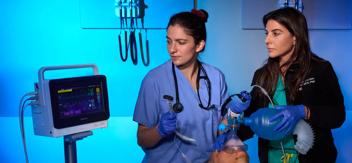 Two clinicians demonstrate intubation and manual ventilation on a medical mannequin while monitoring vital signs on a Philips screen.
