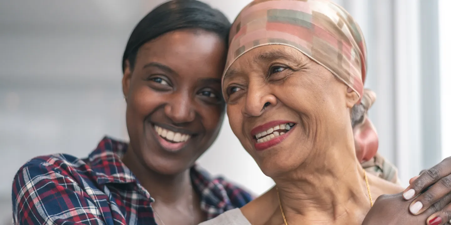 Young woman smiling with her arm around an older woman wearing a headscarf, symbolizing love and support during cancer treatment