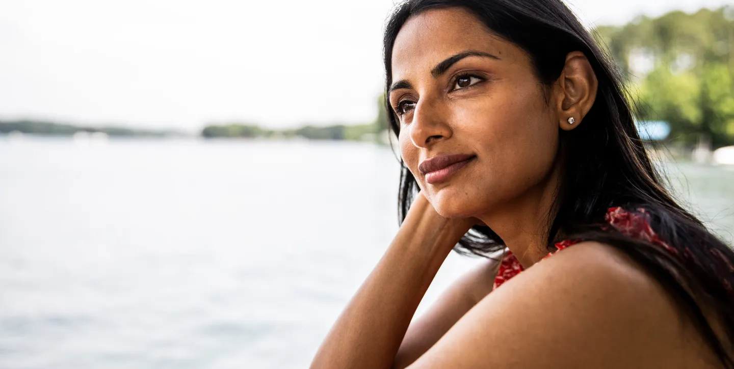 Woman relaxing outdoors near a lake, gazing thoughtfully into the distance on a sunny day