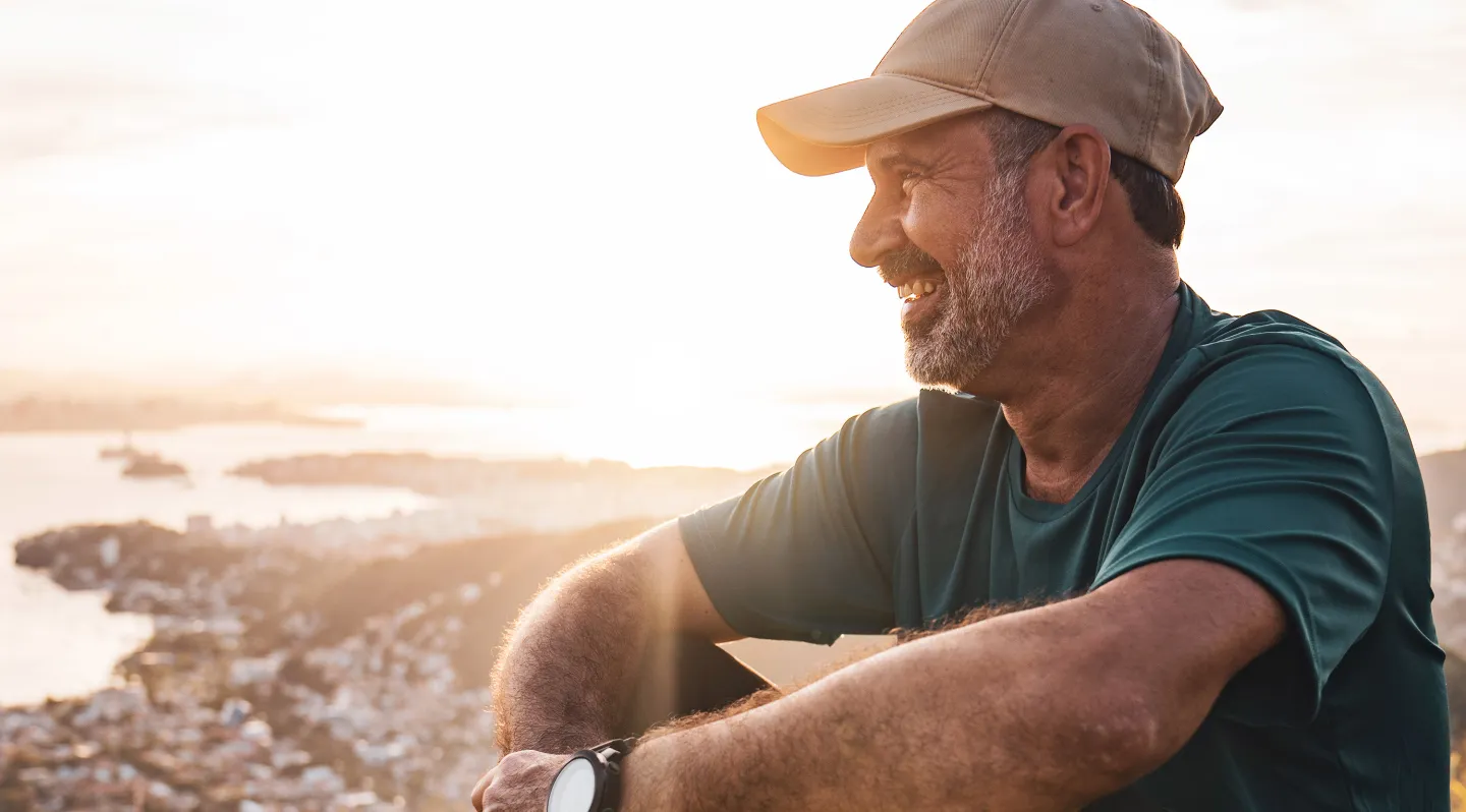 Smiling man in a cap enjoying a scenic view at sunset from a high vantage point.