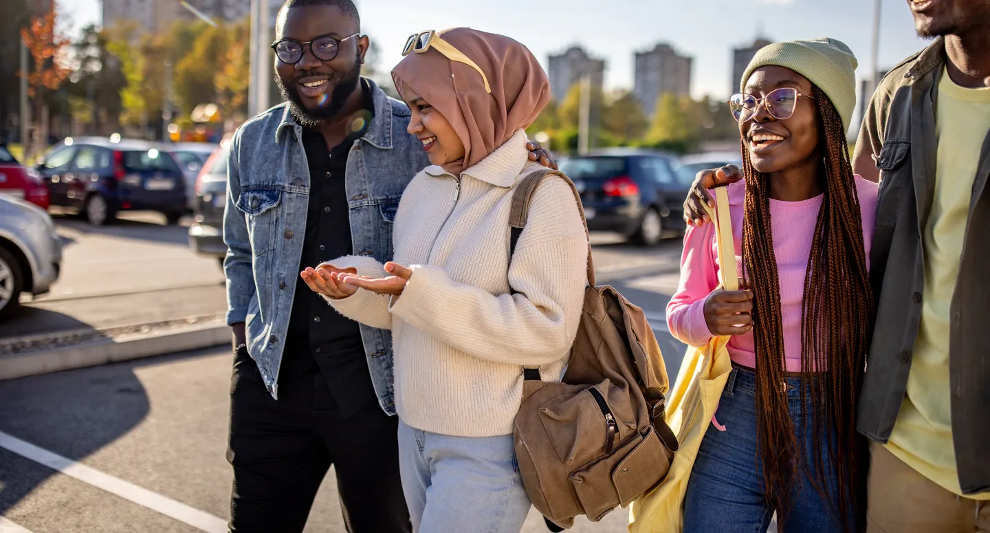 Group of young adults smiling and chatting while walking together in a sunny parking area.