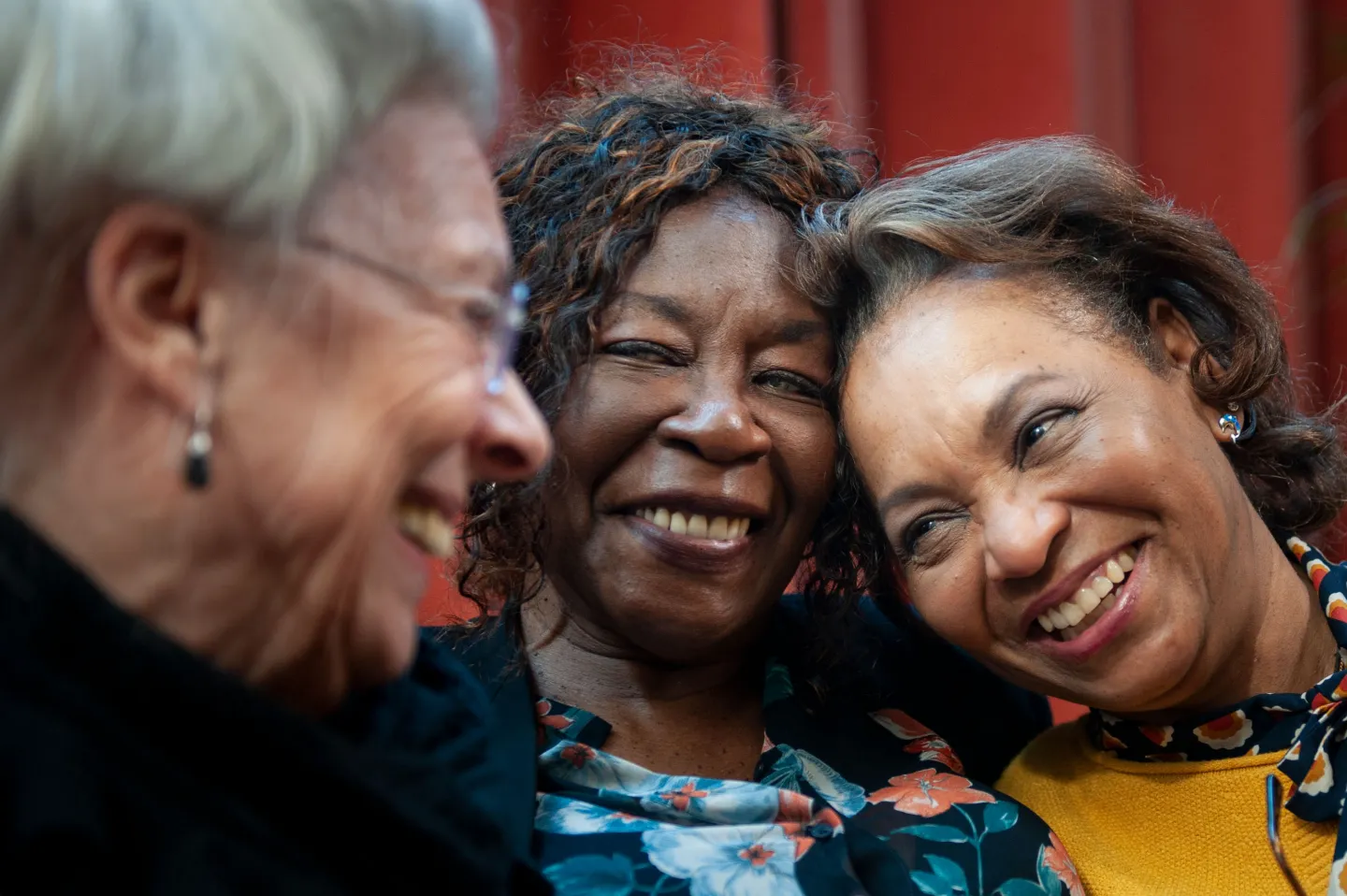 Three older women smiling and leaning in close while laughing together