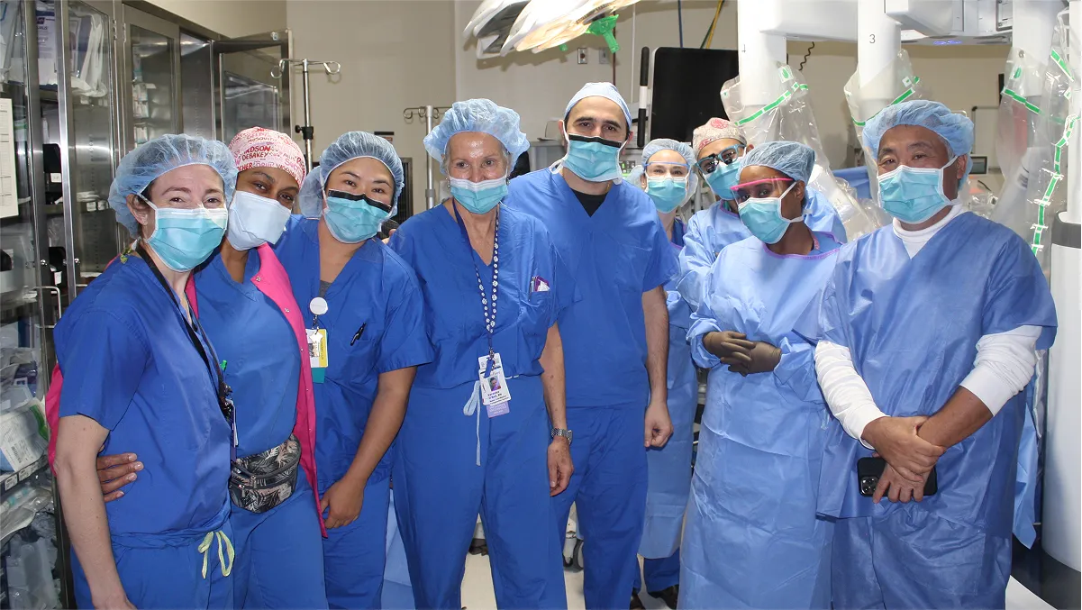 A team of doctors and medical professionals in blue surgical scrubs and masks pose for a group picture.