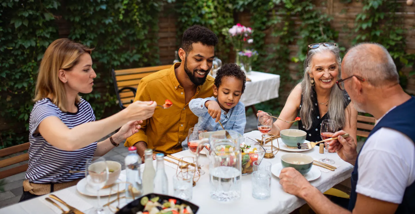 Family sharing a meal outdoors around a table in a garden