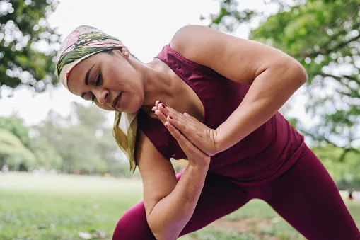 Woman wearing workout clothes and headscarf practices yoga in a park