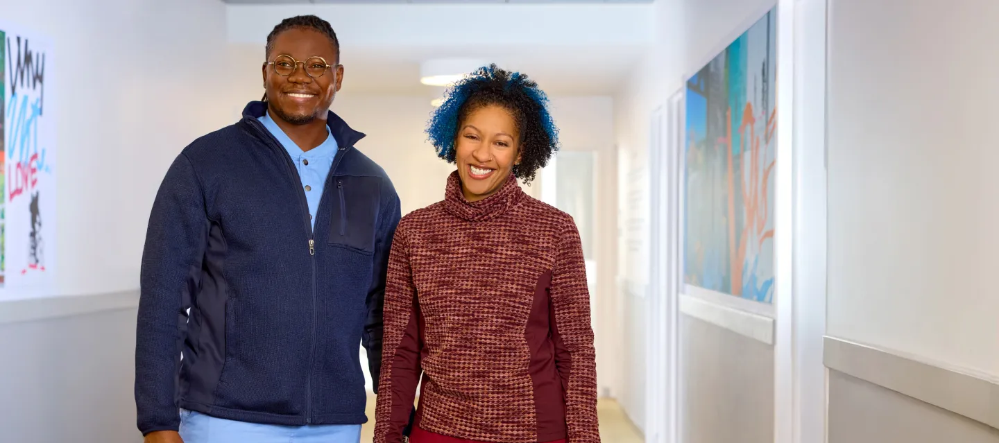 A man and a woman smiling and standing in a hallway
