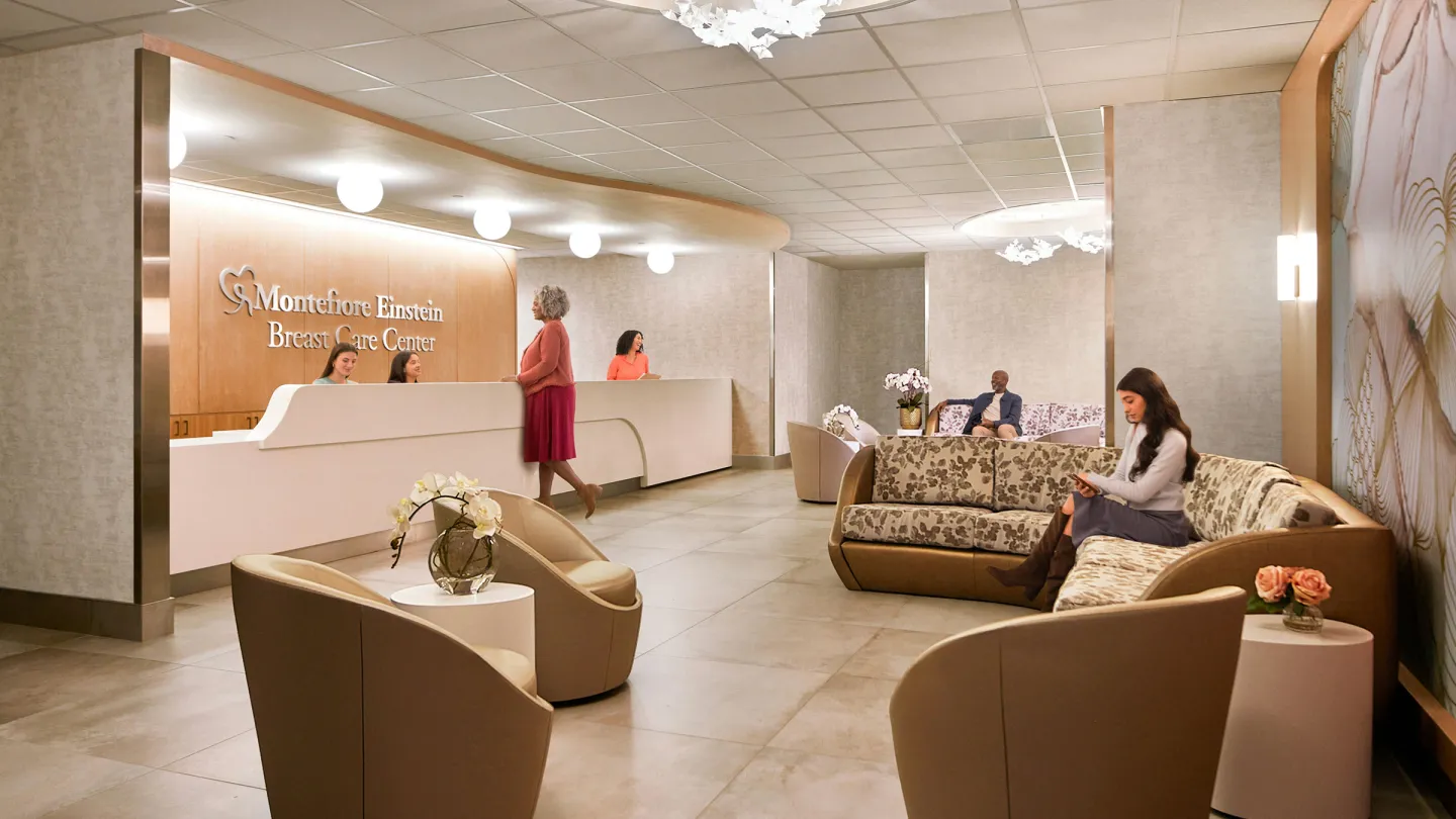 Lobby of the Montefiore Einstein Breast Care Center, with patients seated on curved sofas and staff greeting a visitor at the reception desk.