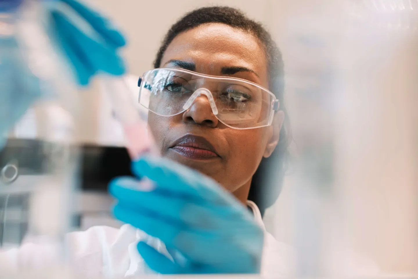 Scientist wearing safety goggles and blue gloves examines a test tube in a laboratory setting