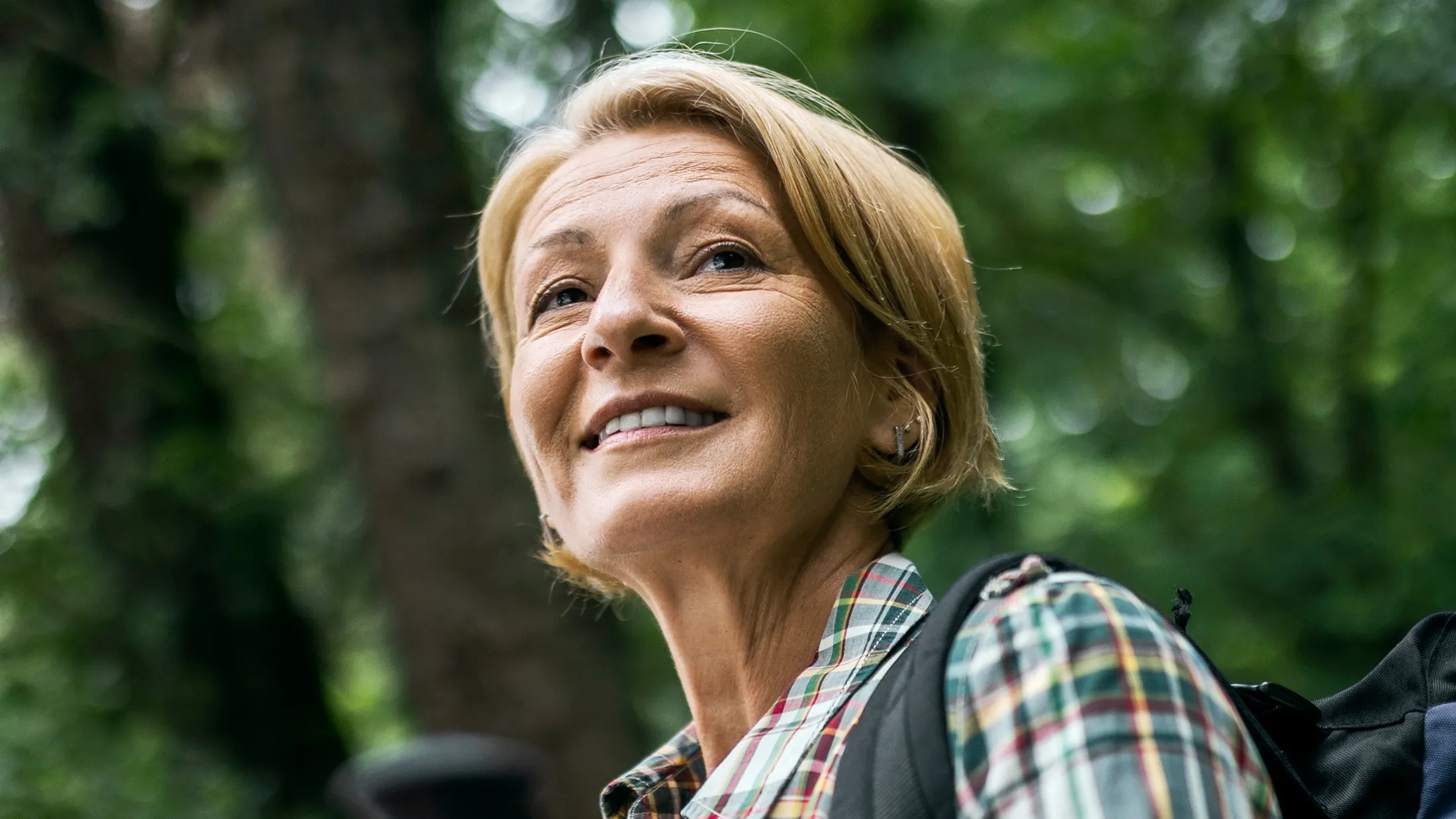 A middle aged adult woman in the forest hiking with hiking poles.