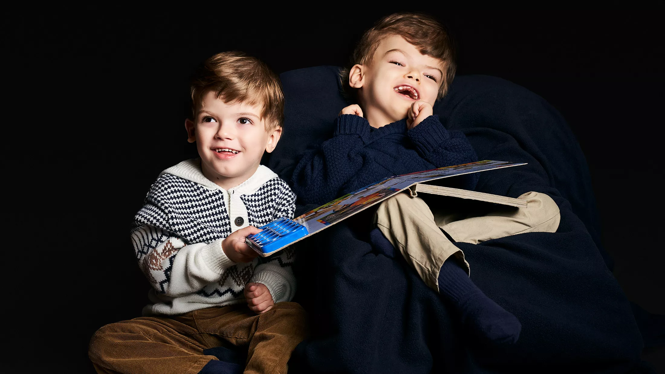Two twins, Jadon and Anias, smiling while sharing a book