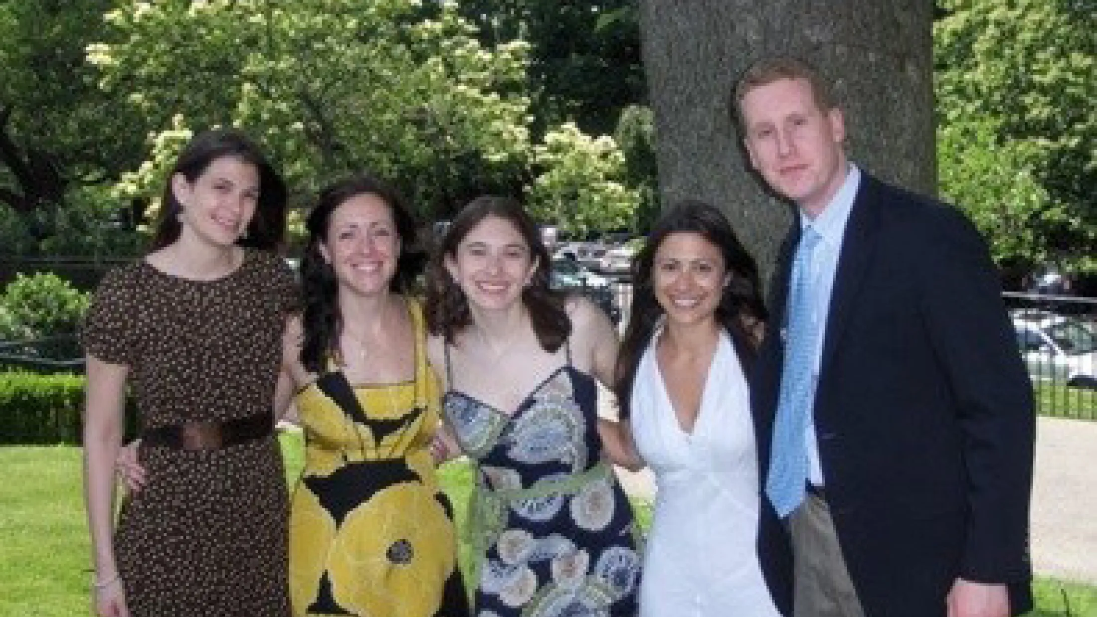 Five people posing outdoors in formal attire with trees and grass in the background.