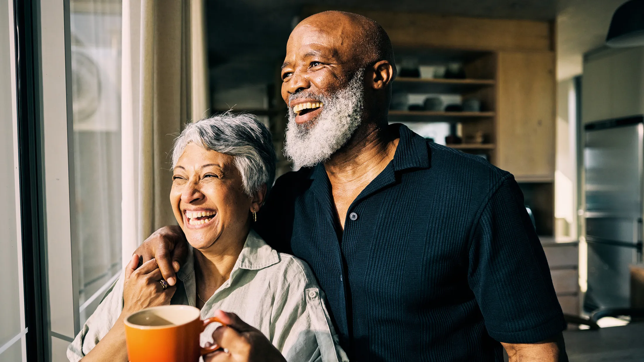 Older couple smiling and looking out a window together, enjoying a peaceful morning at home