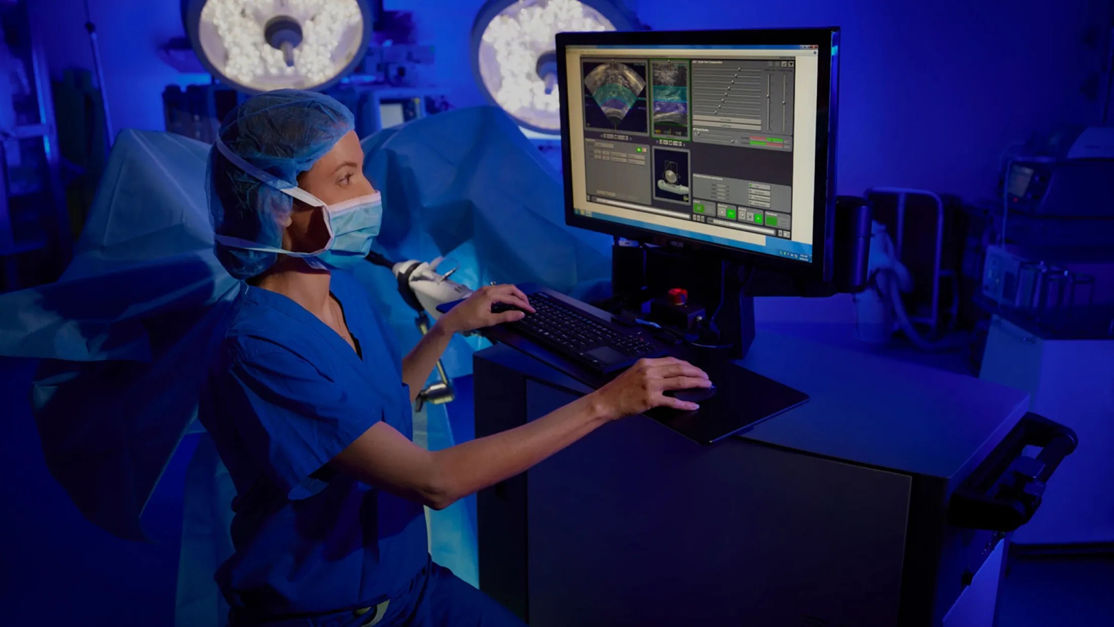 Medical professional in surgical scrubs operating a computer system in a high-tech operating room.