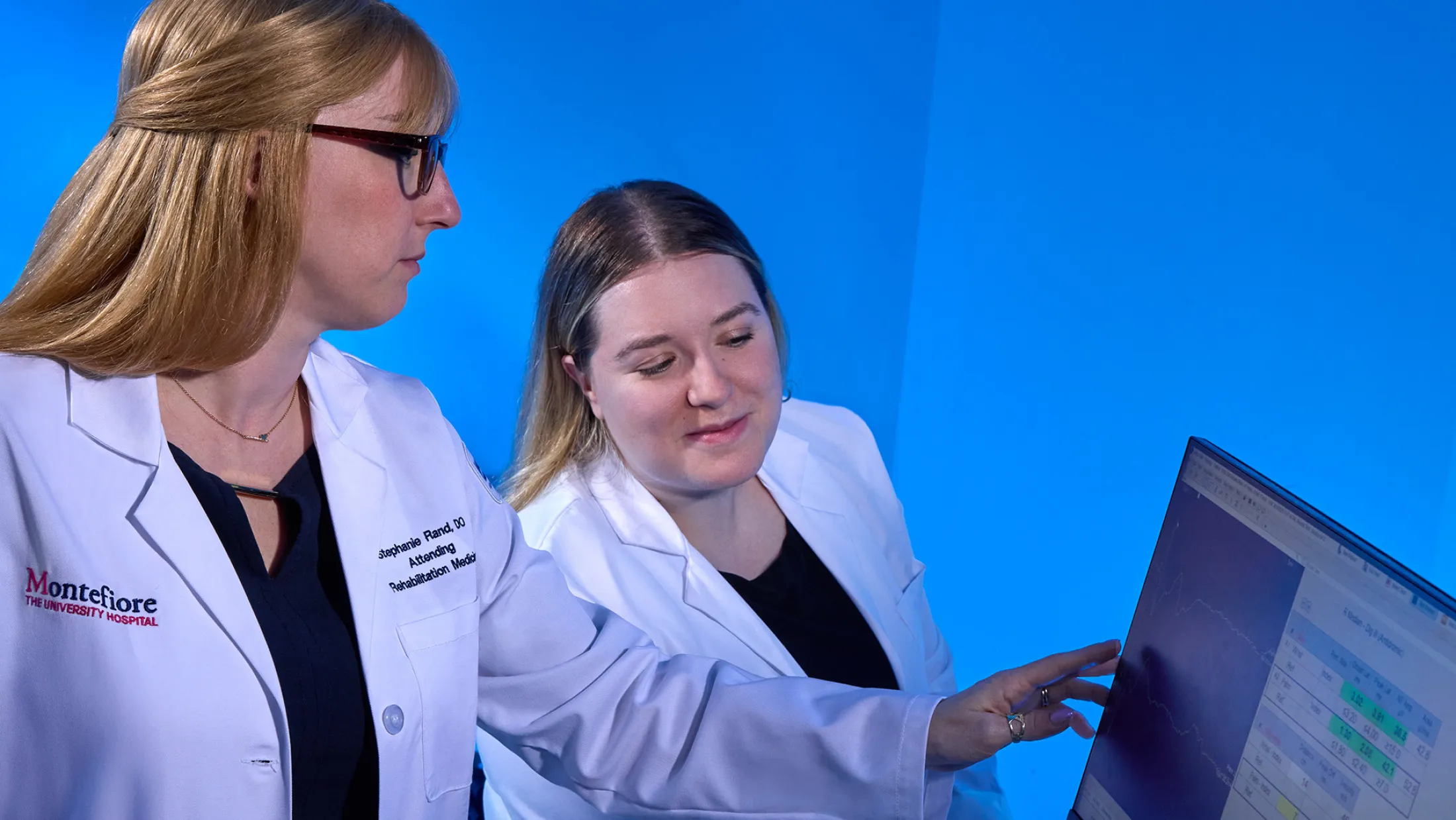 Two female medical professionals reviewing nerve conduction data on a computer screen in a clinical setting.