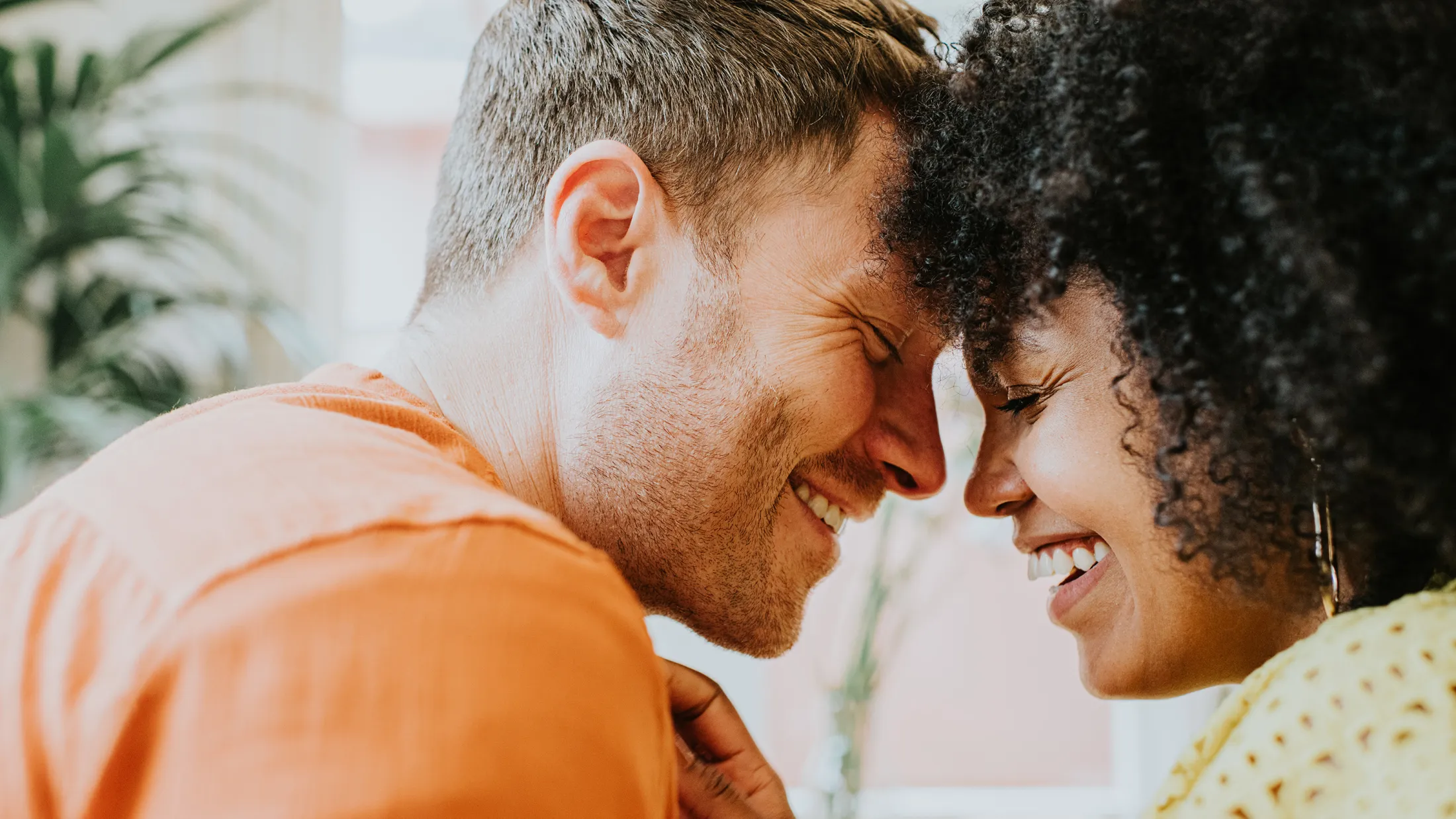 A joyful couple sits closely, smiling and touching foreheads, sharing an intimate and happy moment together.