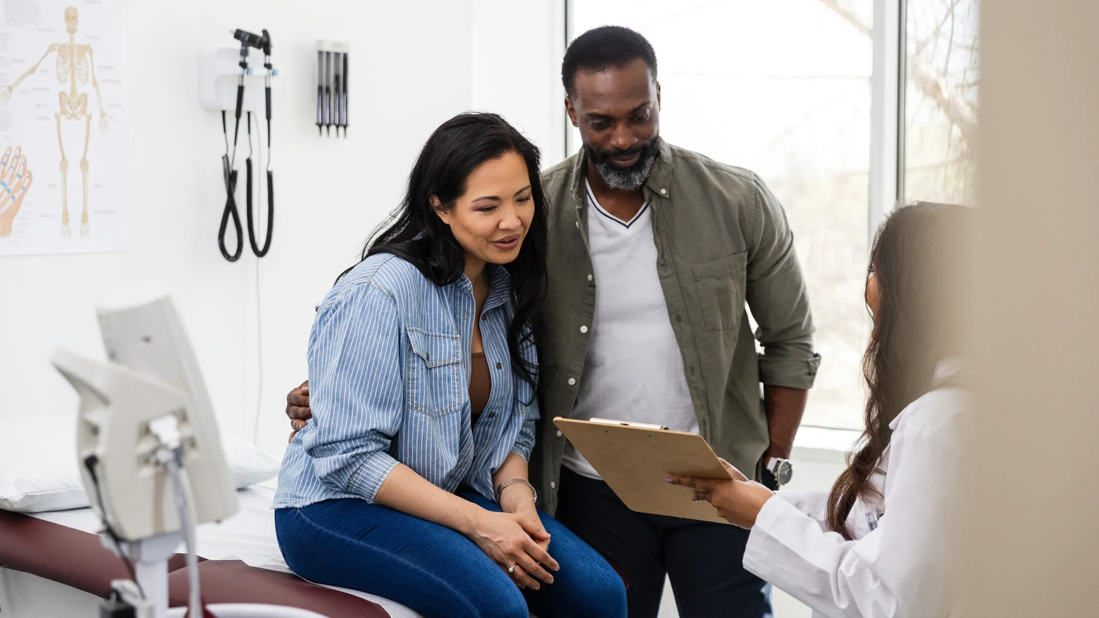 Couple speaking with a female doctor during a medical consultation in a bright examination room.