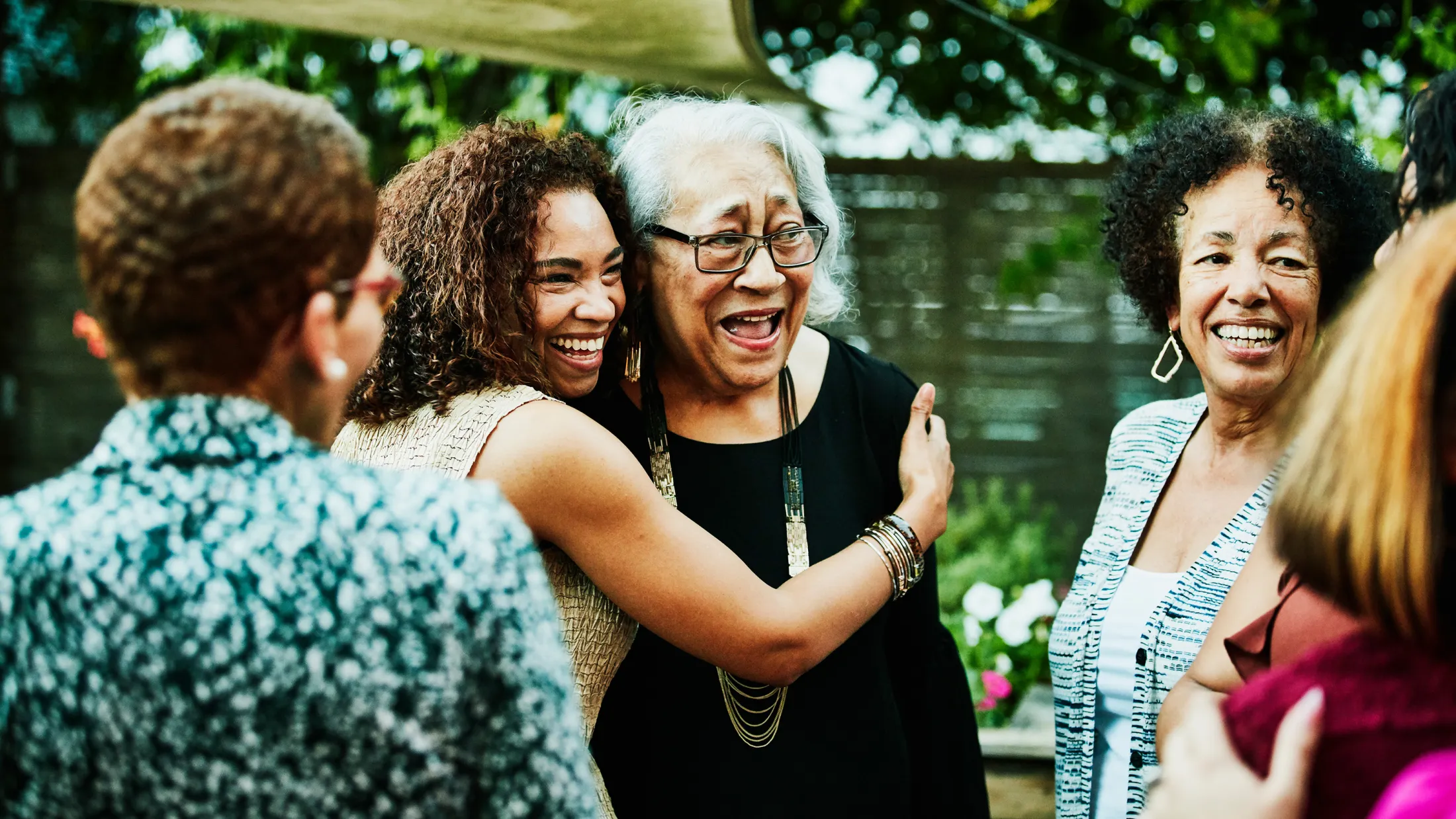 Elderly woman laughing as she is embraced by a younger woman at a joyful gathering.