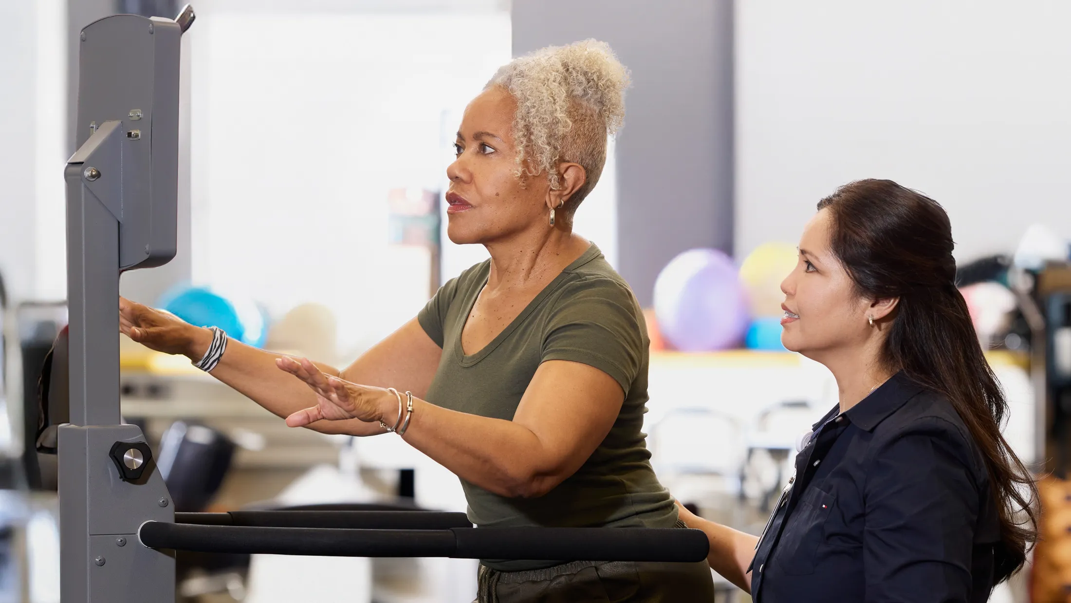 Older woman using a rehabilitation treadmill with assistance from a physical therapist.