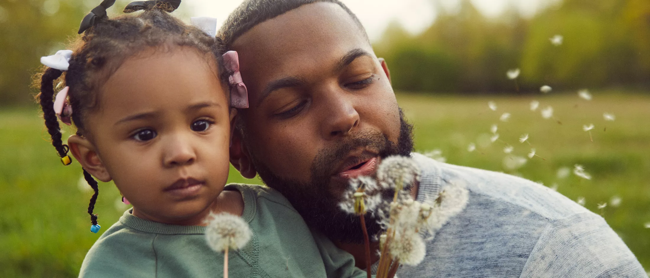 A man blowing dandelions with his daughter outside