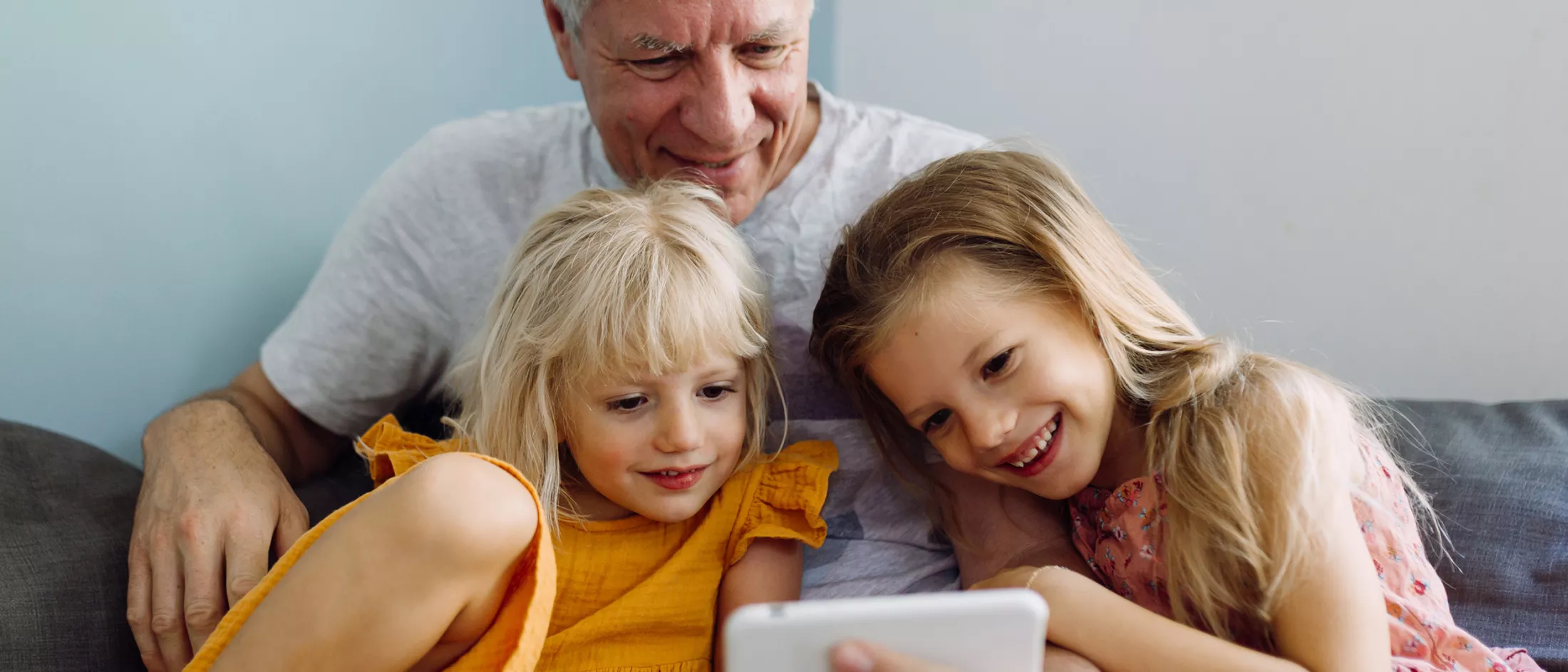 Two sisters and their grandfather laughing and having good time while using a mobile phone