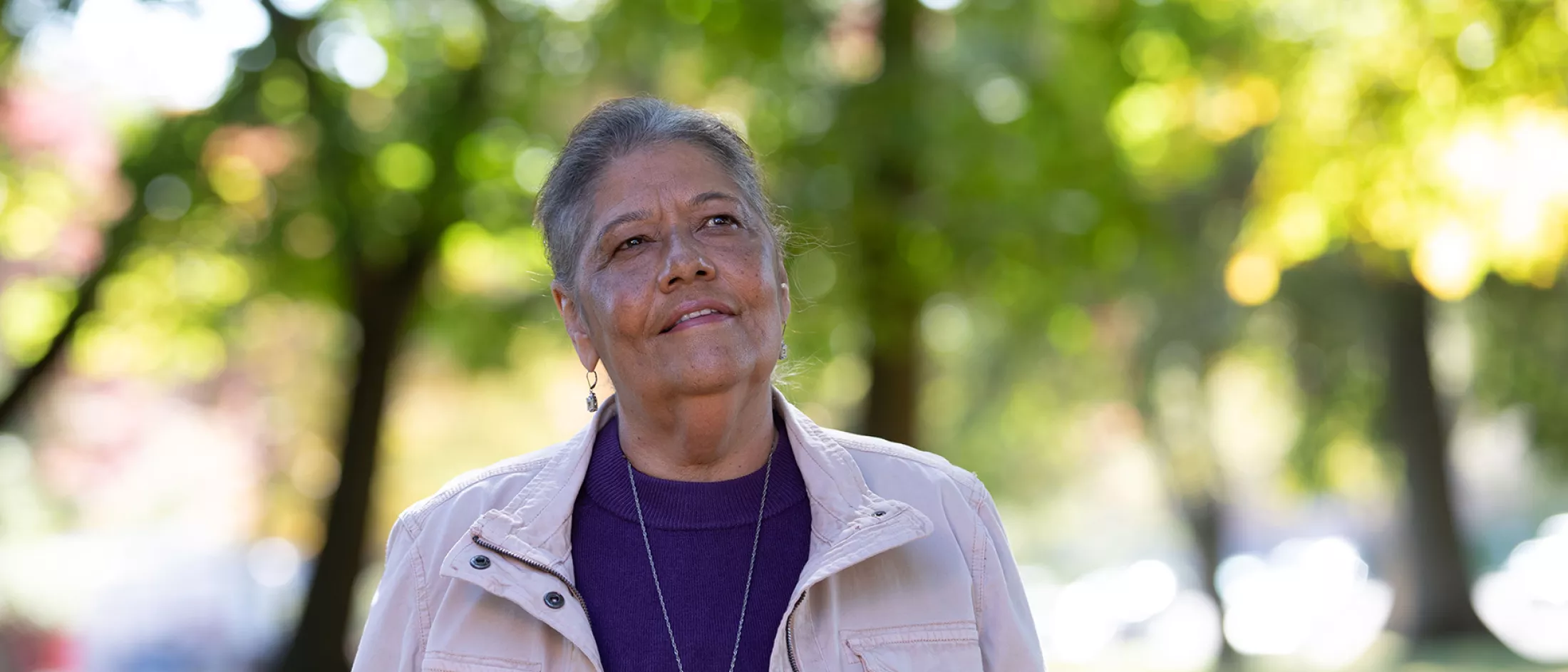 A woman outside looking up at the trees