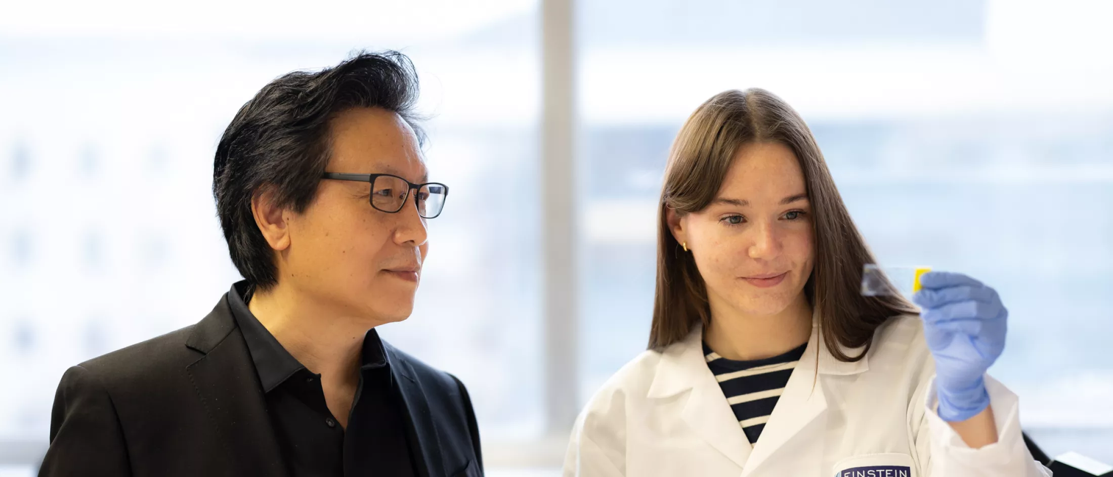 Dr. Xingxing Zang reviews a slide with a female researcher in a white lab coat.
