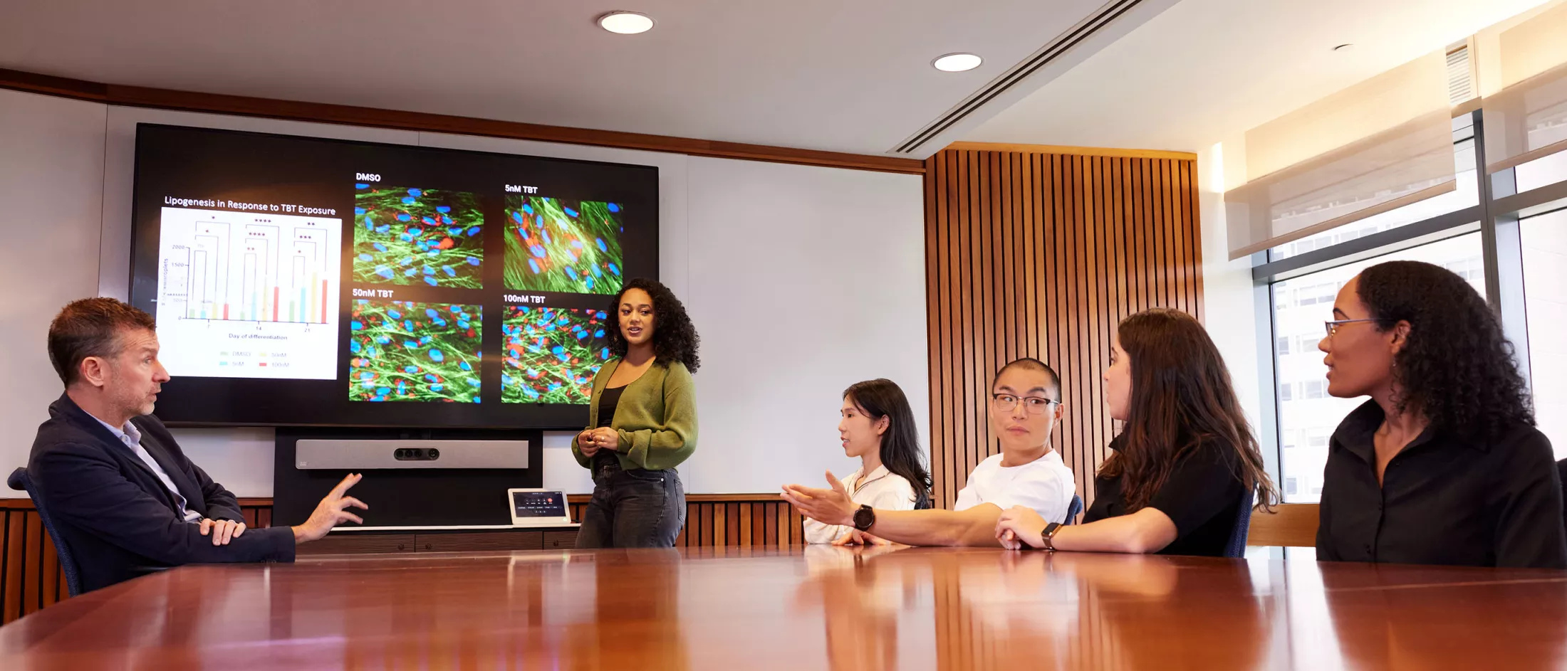 A group of professionals engaged in discussion around a large conference table in a modern meeting room.