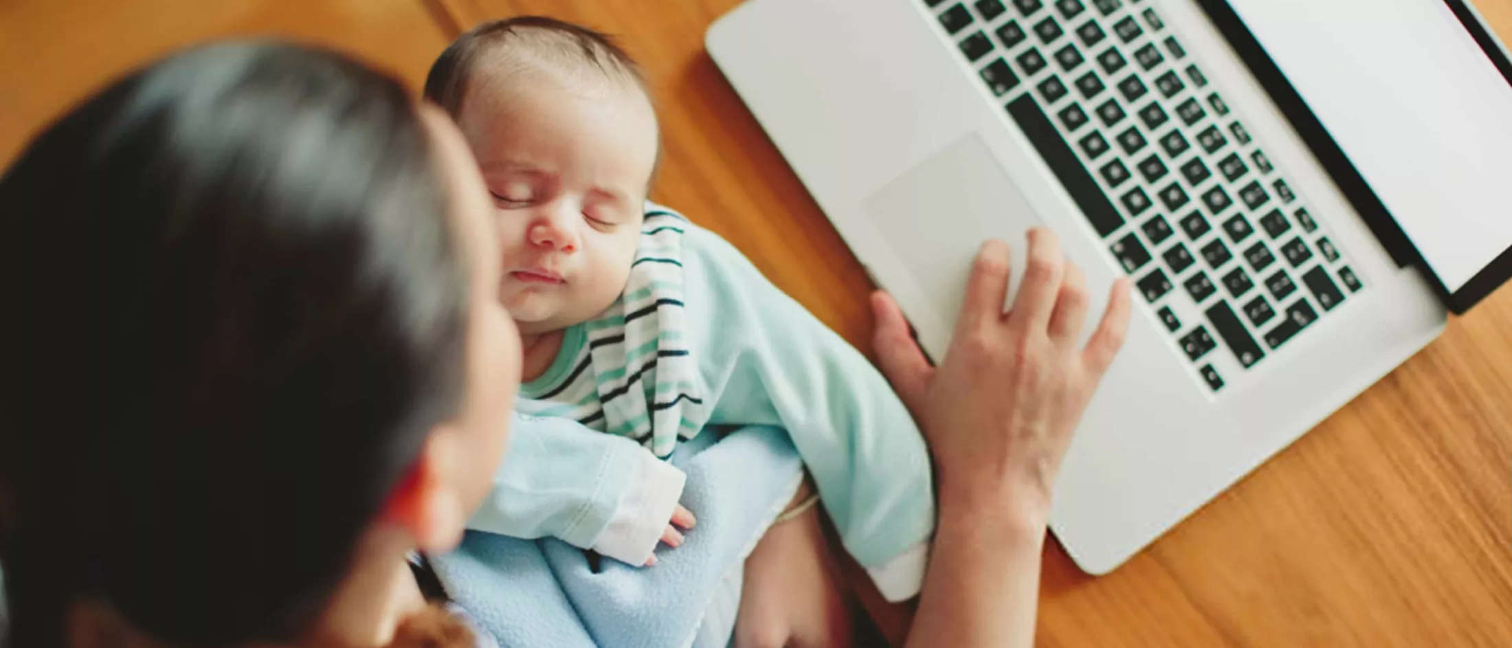 Mother holding sleeping baby while using laptop