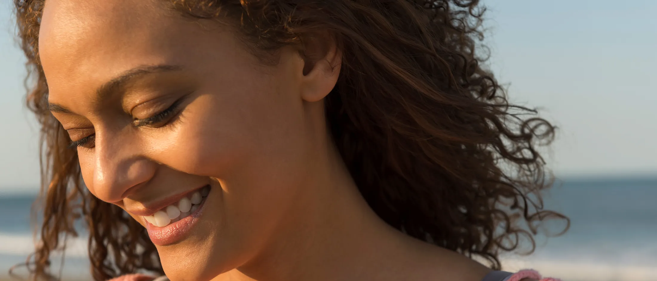 Smiling woman with curly hair enjoying sunlight at the beach