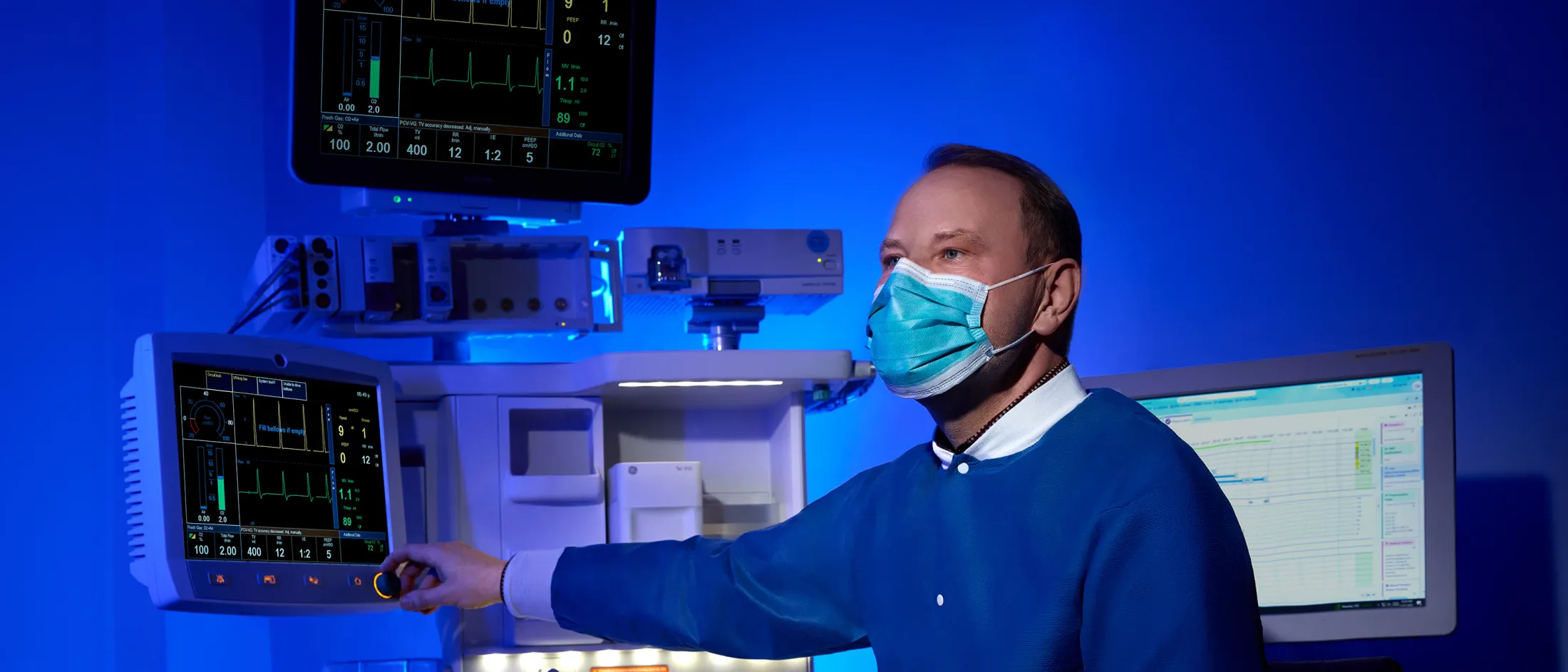 Medical professional adjusting monitor in a blue-lit surgical environment