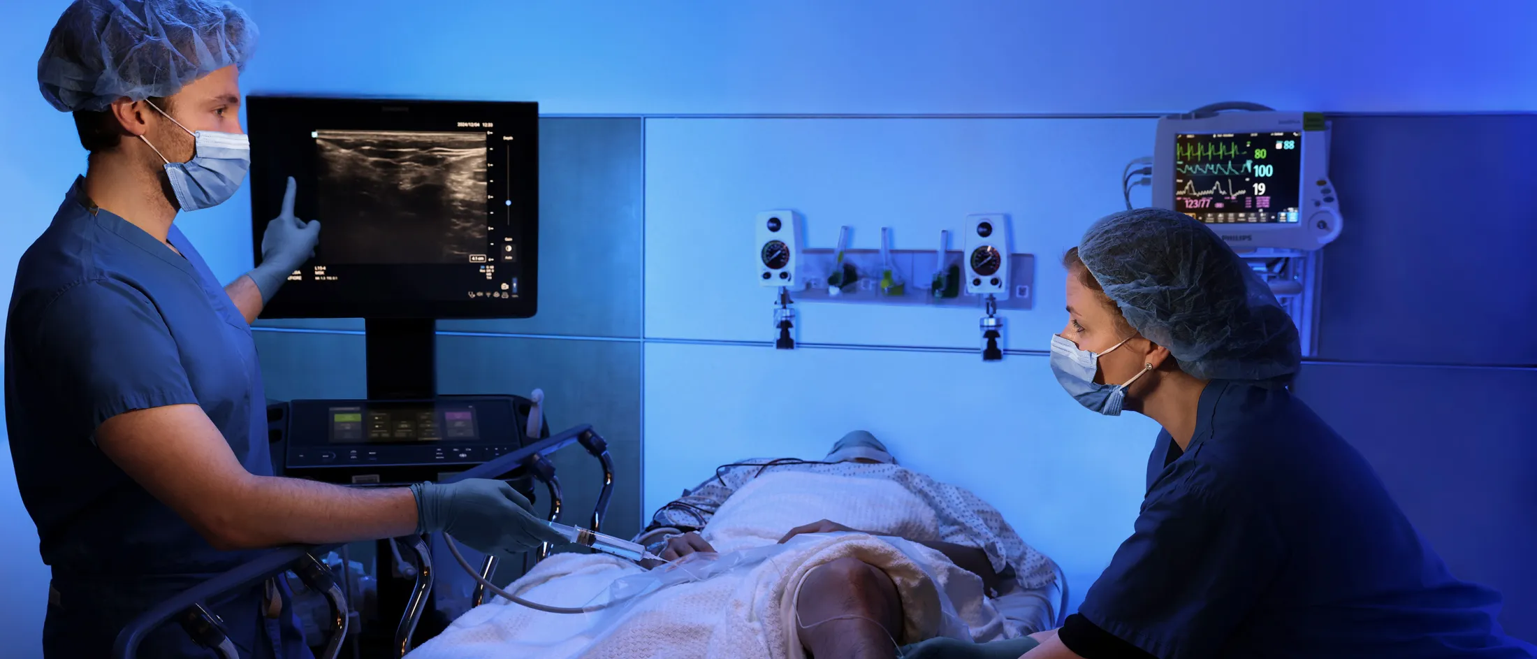 Medical professionals perform an ultrasound-guided procedure on a patient's leg in a hospital setting.