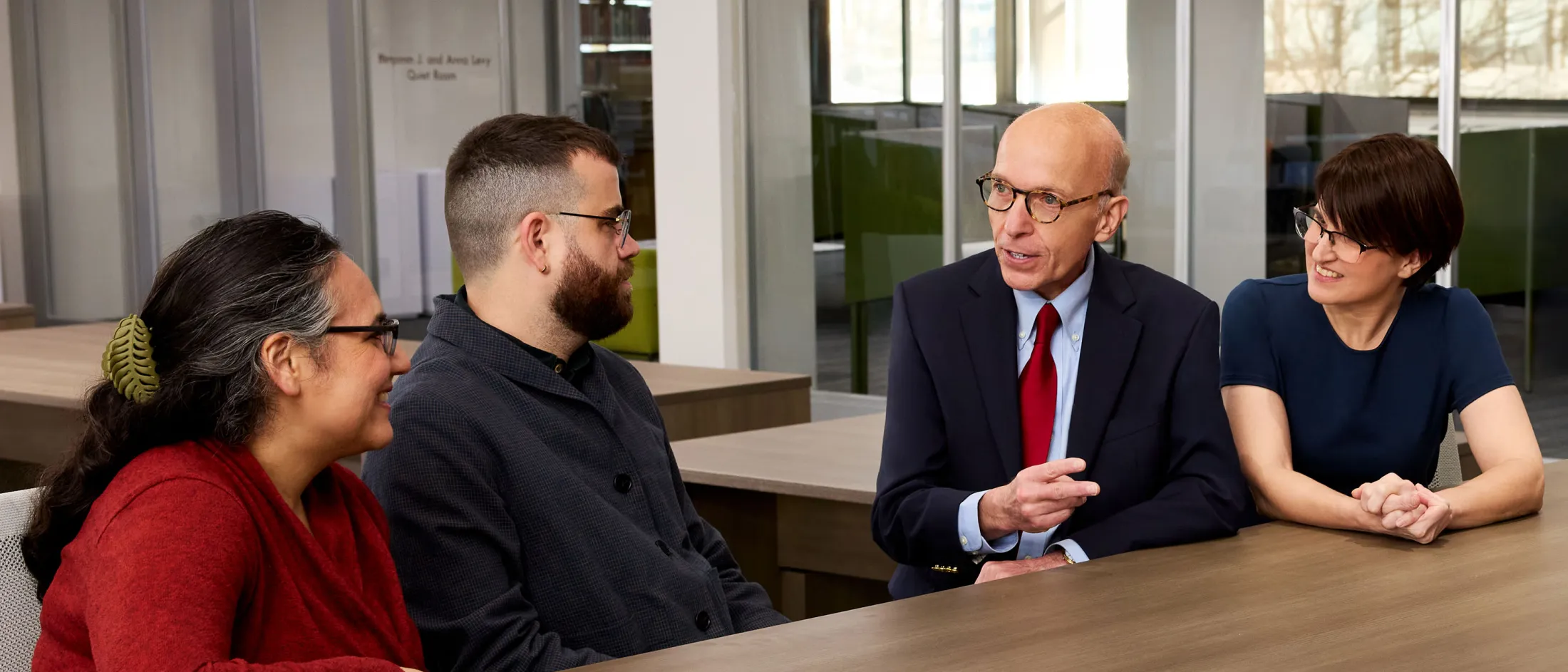 Four colleagues sit together at a table in a modern office, engaged in a lively and friendly discussion.