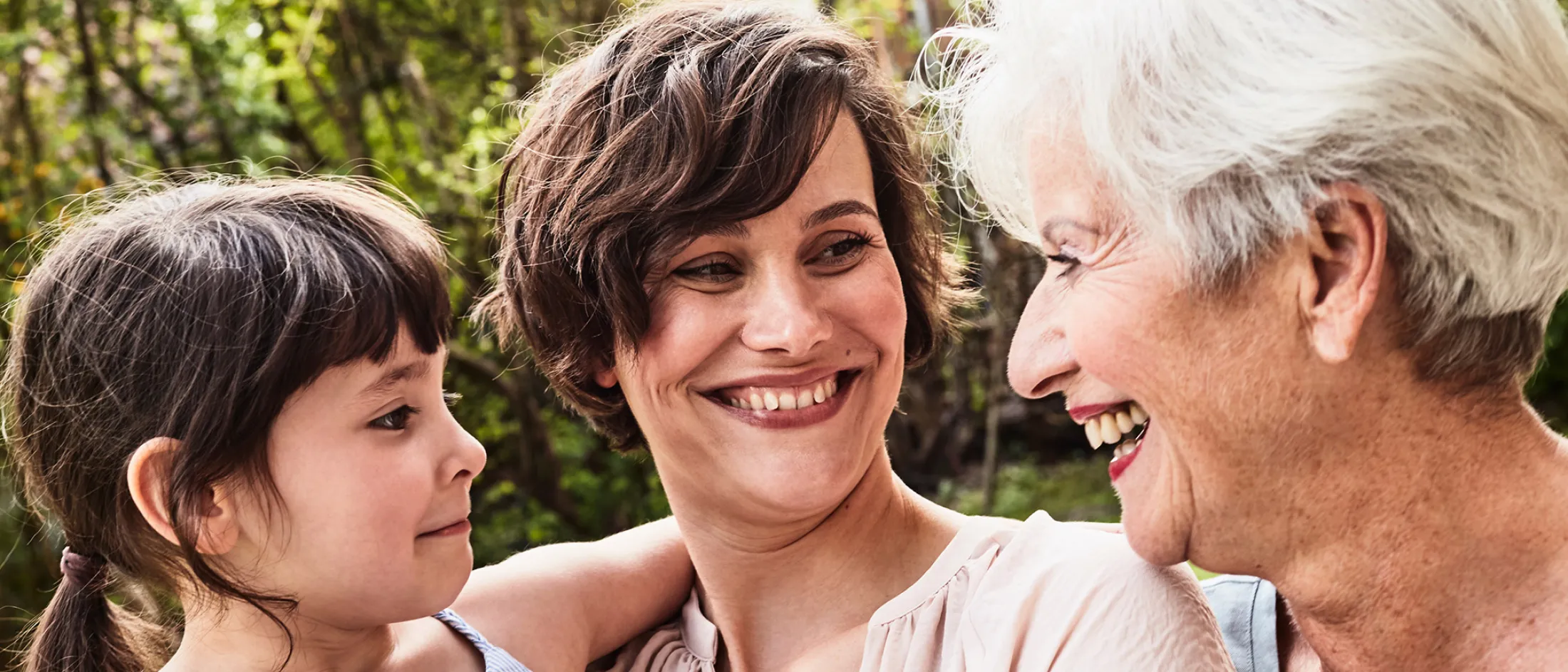 Three generations of women—child, mother, and grandmother—smiling and enjoying time together outdoors.