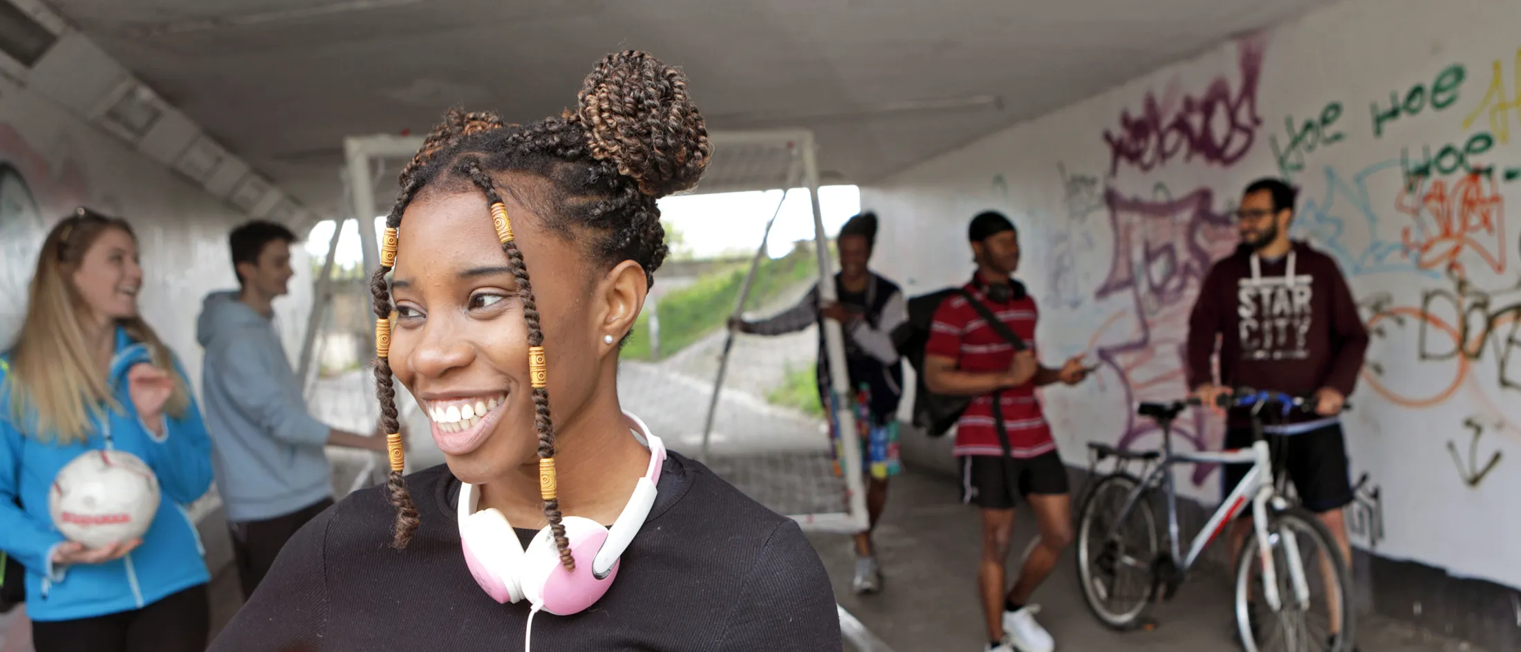 Teen girl holding a soccer ball with friends and graffiti wall in the background