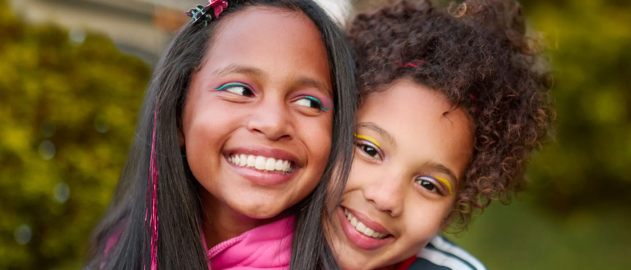 Two young girls smiling and hugging while playing outside