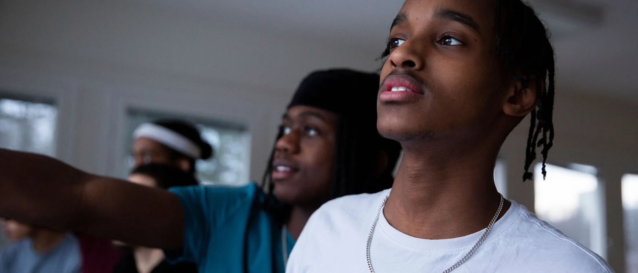 Teen boys looking ahead while one points, standing indoors with natural light