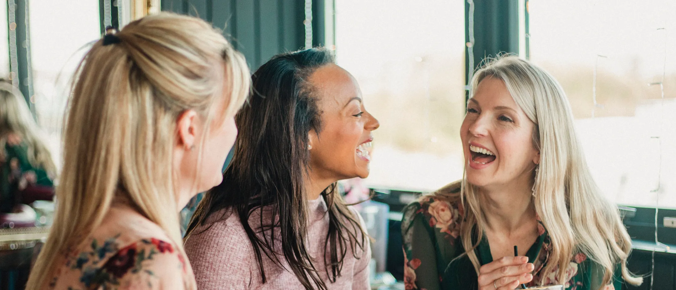 Three women laughing and enjoying a meal together at a restaurant