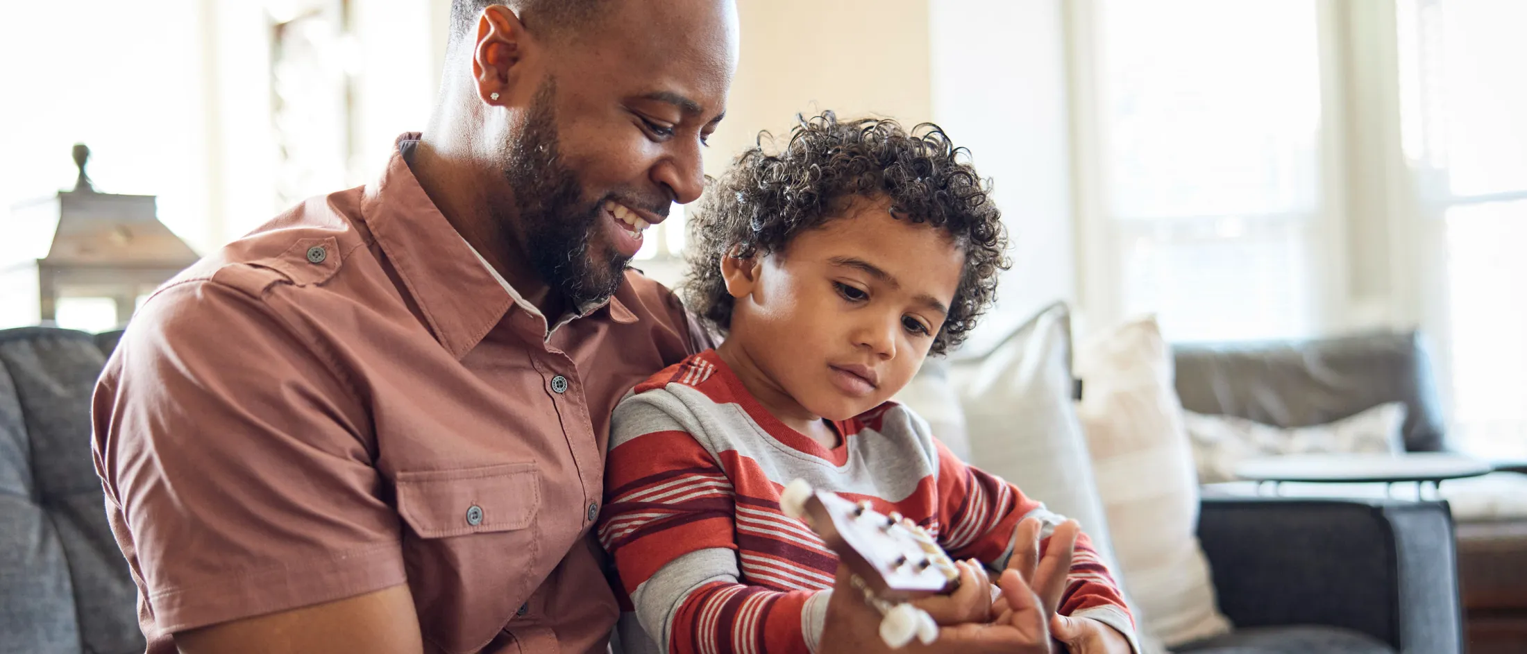 Father teaching his young son to play ukulele in a cozy living room