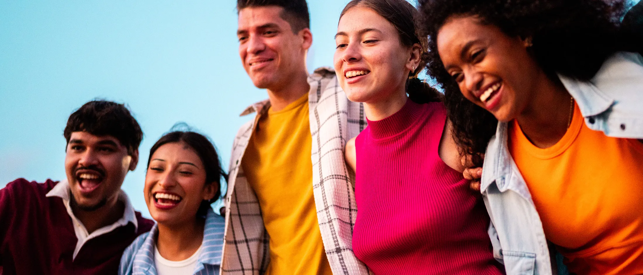 Group of five young people smiling and standing together outdoors