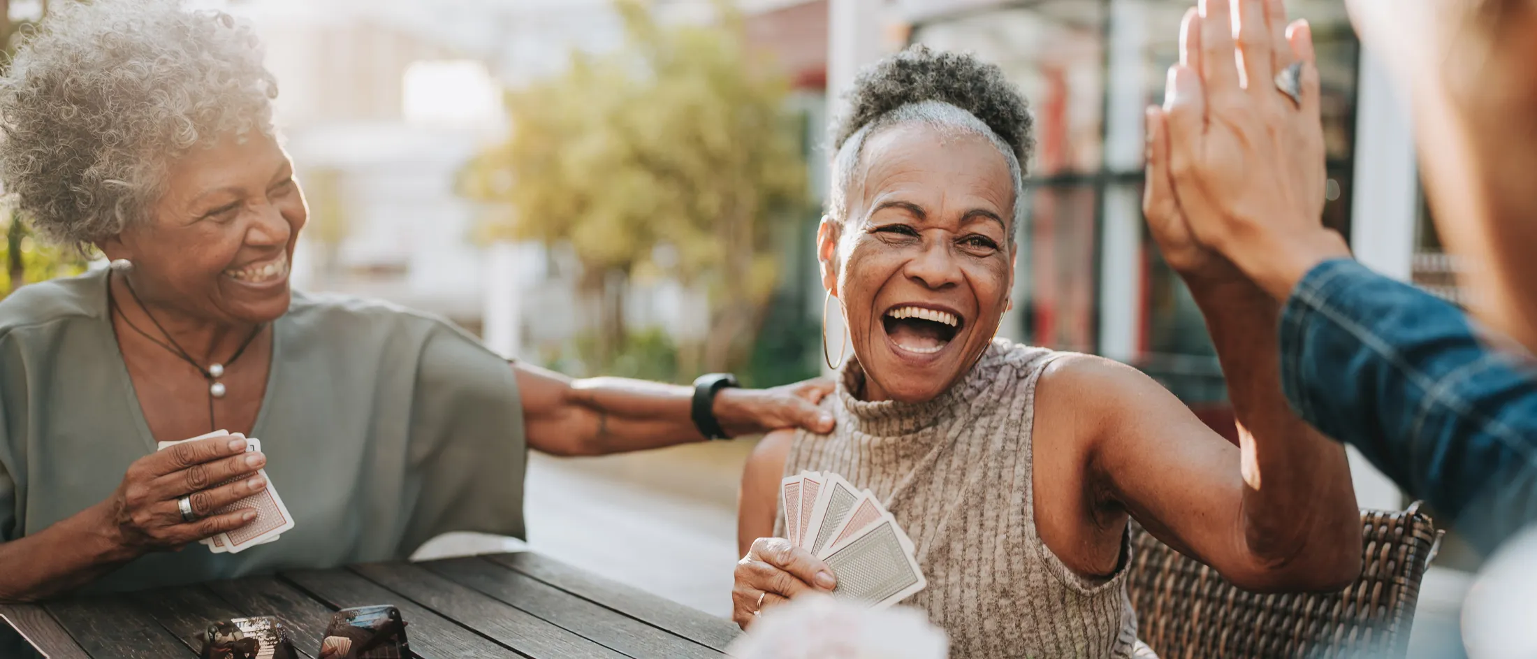 Group of older women laughing and playing cards outside