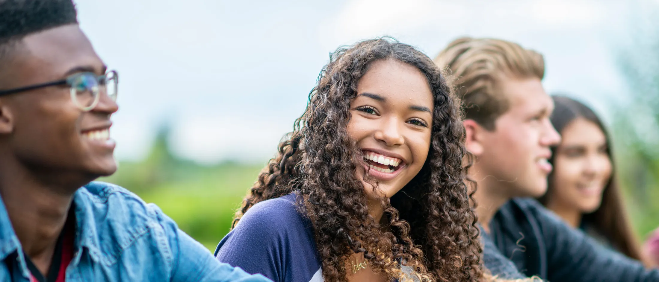 Happy teenage girl smiling while sitting with a group outdoors