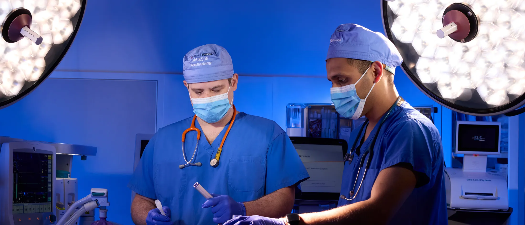 Two anesthesiologists in blue scrubs prepare for surgery in an operating room with advanced equipment.